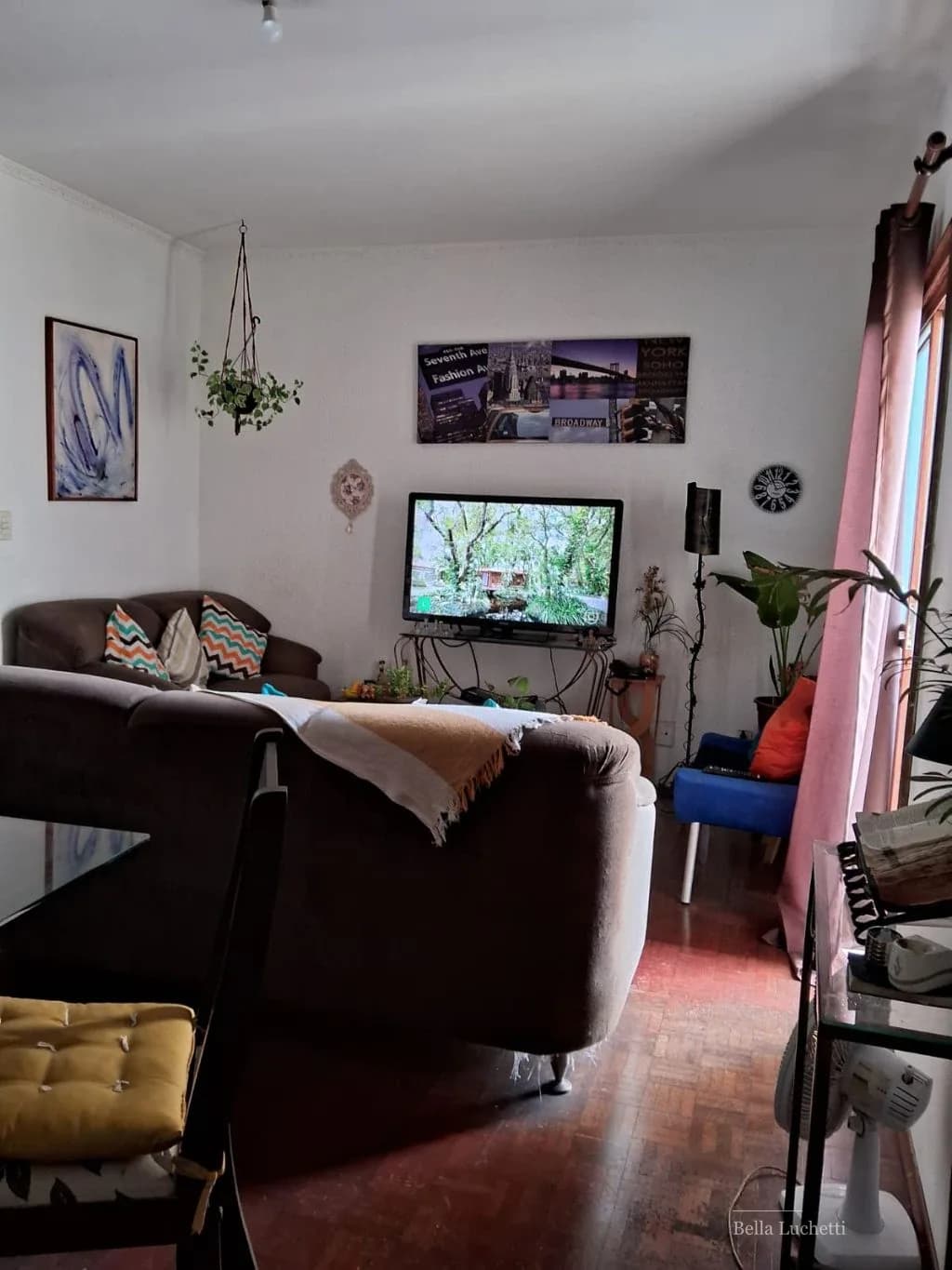 Vista ampla da sala mostrando sofá, TV, mesa de jantar e decoração com plantas.